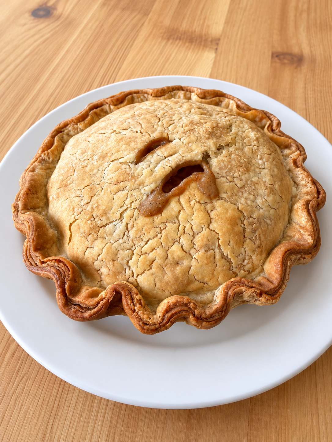 Un pâté à l'oie entier à la croûte dorée et festonnée, sur une assiette blanche.