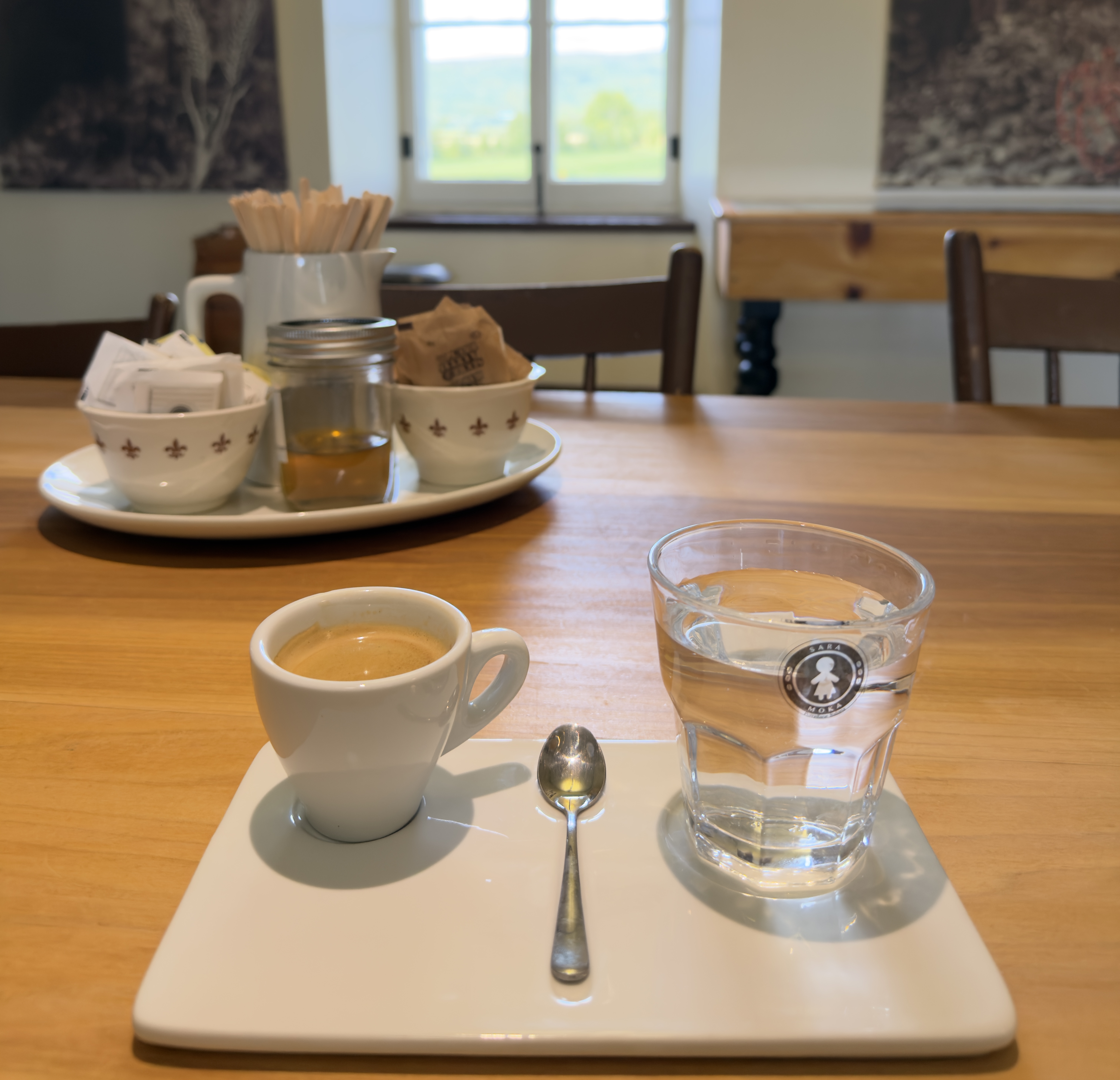Un espresso et un verre d'eau sur une table du café du Musée, devant une fenêtre et des photos d'archives.