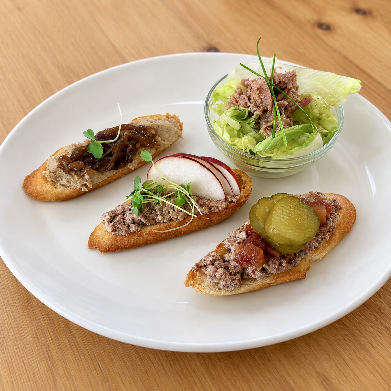 Assiette dégustation : trois croûtons garnis de terrine, de mousse et de rillettes d'oie, avec confit d'oignons, radis, cornichon et petite salade.